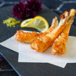 Three Jumbo Shrimp Tempura on a black plate with matcha salt and a lemon slice.
