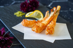 Three Jumbo Shrimp Tempura on a black plate with matcha salt and a lemon slice.
