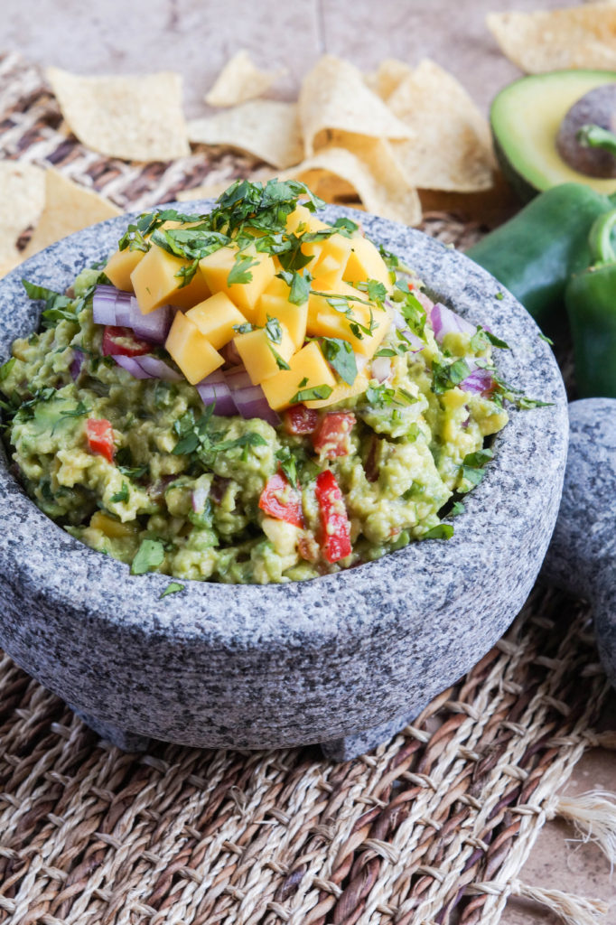 Mango Guacamole Close up of Mango Guacamole in a Molcajete with tortilla chips in the background.