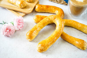 Meitschibei (Swiss Horseshoe-Shaped Pastries) next to a cup of coffee and pink flowers.