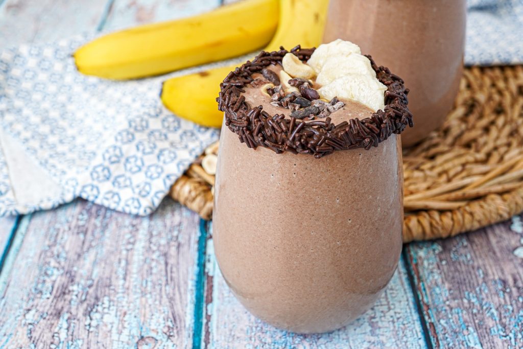 Side view of Chocolate Peanut Butter Smoothie in two glasses next to two bananas.