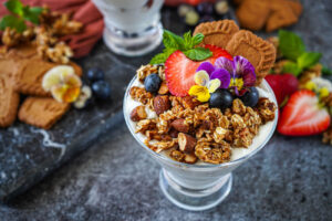 Cookie Butter Granola over yogurt in a glass with strawberries, blueberries, pansies, and Biscoff cookies.