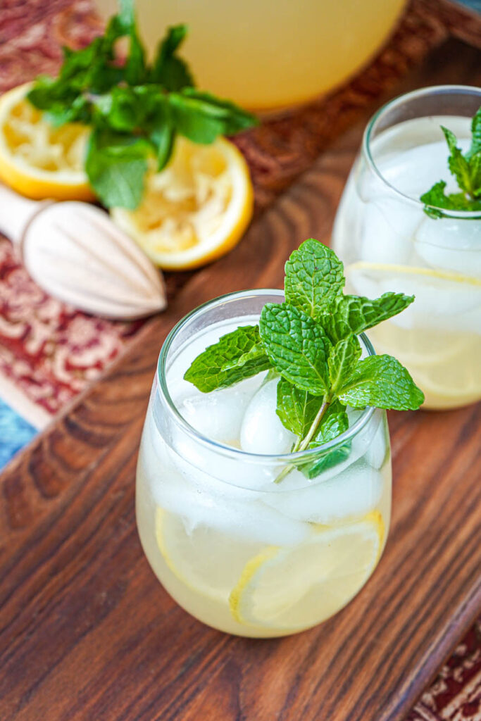 Shikanji (Indian Spiced Lemonade) in two glasses with lemon halves and fresh mint in the background.