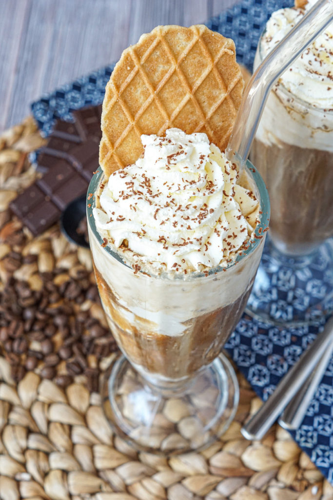 Close up of Eiskaffee in a tall glass with straw, whipped cream, and a waffle cookie.