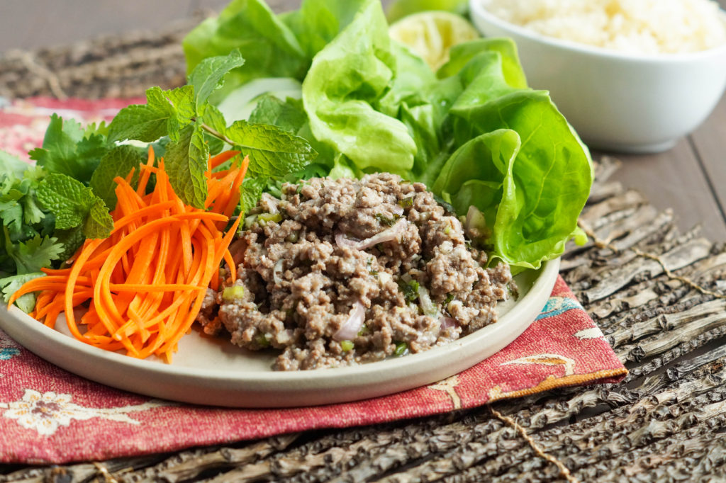 Laab Nua (Thai Spicy Beef with Mint Leaves) on a tan plate with sliced carrots, mint, and lettuce.