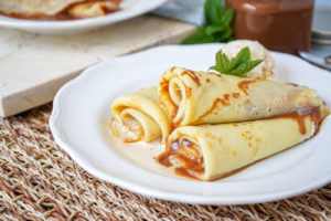 Three rolled Panqueques con Dulce de Leche (Argentinian Dulce de Leche Crepes) on a white plate.