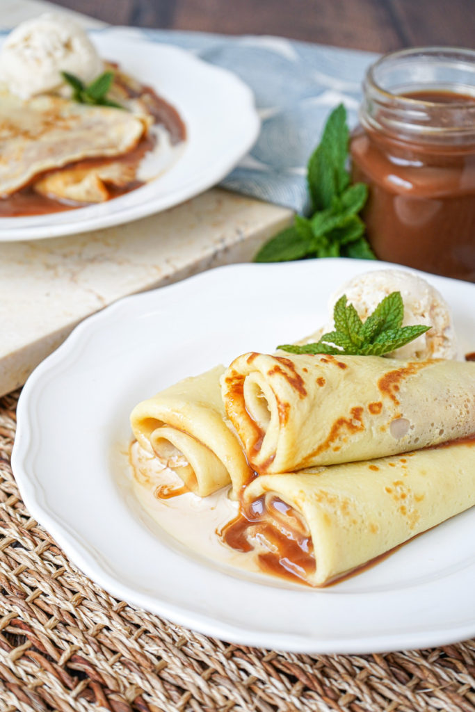 Side view of three rolled Panqueques con Dulce de Leche (Argentinian Dulce de Leche Crepes) on a white plate.