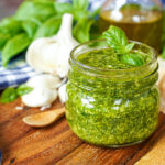 Pistou (Provençal Basil Sauce) in a jar next to bread slices and garlic cloves.