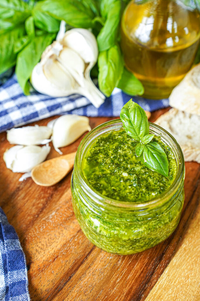 Close up of Pistou (Provençal Basil Sauce) in a jar next to garlic cloves, basil, and bread.