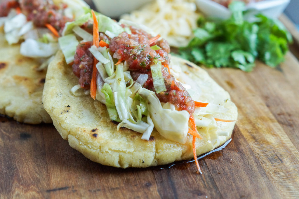 Pupusas de Queso (Salvadoran Cheese-Stuffed Tortillas) on a wooden board and topped with cabbage and salsa.