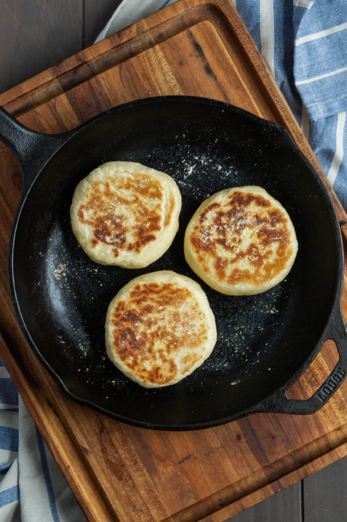 Aerial view of three English Muffins in a cast iron skillet.
