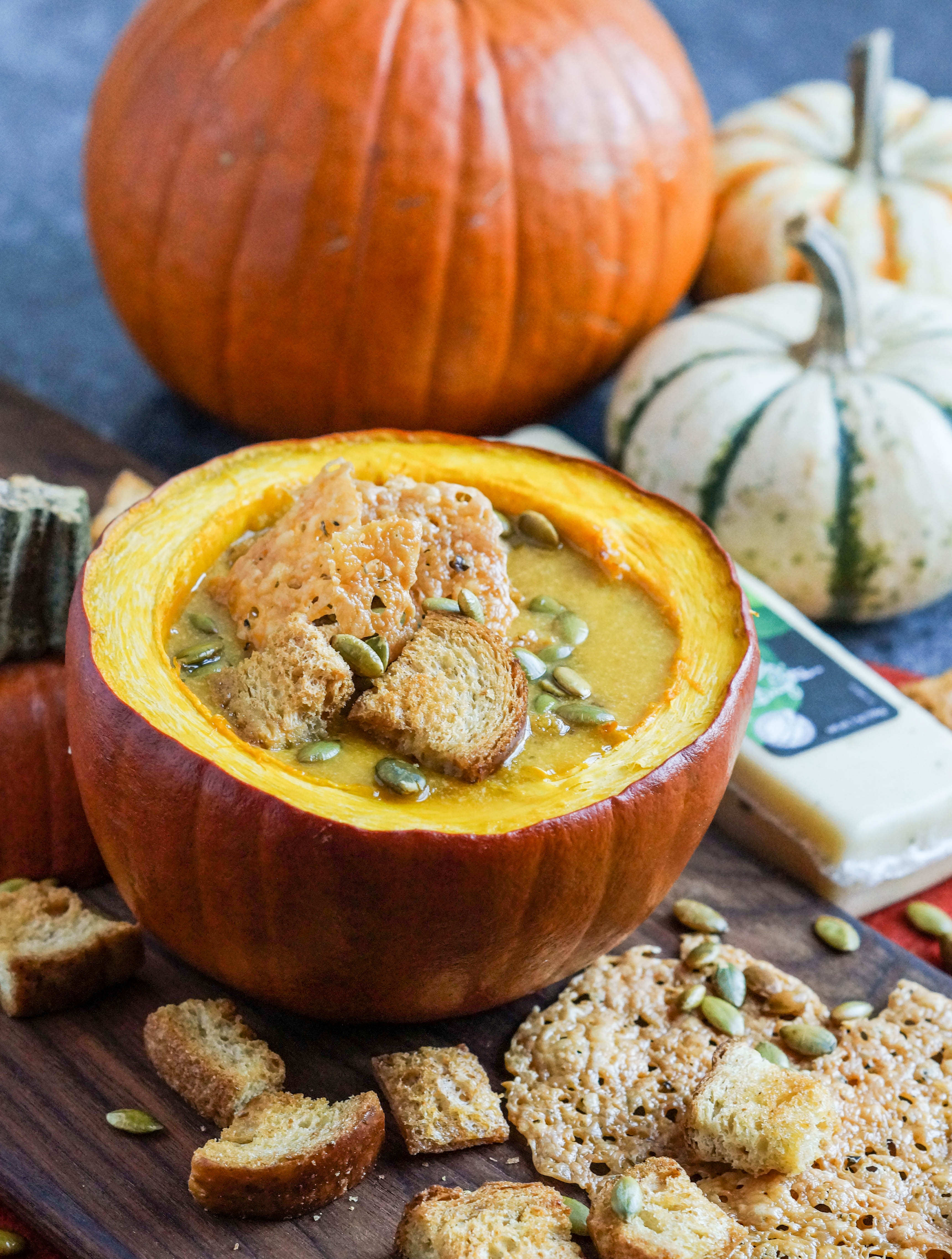 Pumpkin Cheese Soup with Garlic Basil Cheese Crisps in a roasted pumpkin with more pumpkins in the background.