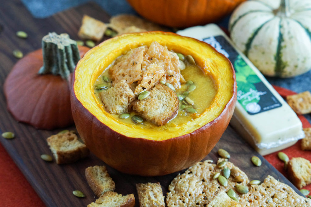 Close up of Pumpkin Cheese Soup with Garlic Basil Cheese Crisps in a roasted pumpkin on a wooden board.