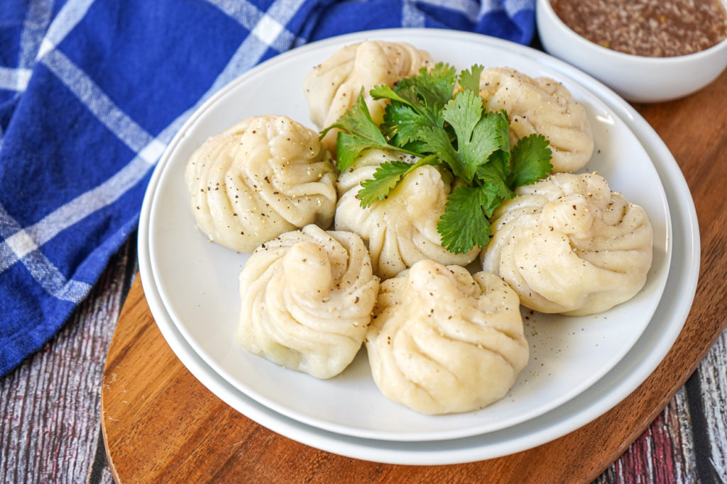 Seven Khinkali (Georgian Topknot Dumplings) on a white plate with fresh cilantro.