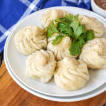 Seven Khinkali (Georgian Topknot Dumplings) on a white plate with fresh cilantro.