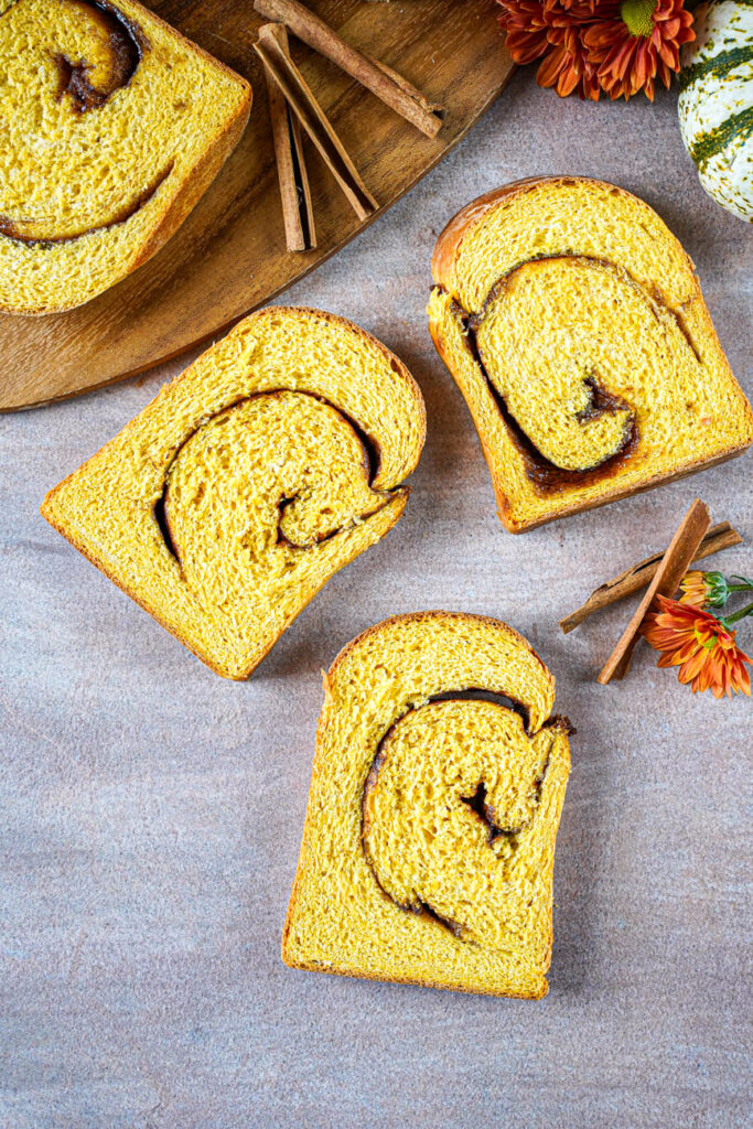 Aerial view of three slices of Pumpkin Cinnamon Swirl Bread next to cinnamon sticks and orange flowers.
