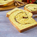 Three slices of Pumpkin Cinnamon Swirl Bread next to cinnamon sticks and orange flowers.
