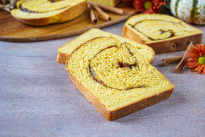 Three slices of Pumpkin Cinnamon Swirl Bread next to cinnamon sticks and orange flowers.