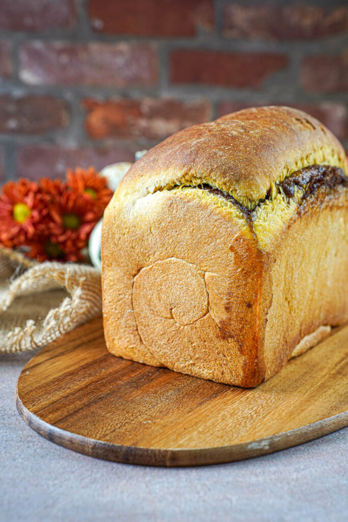 Pumpkin Cinnamon Swirl Bread on a wooden board with orange flowers in the background.