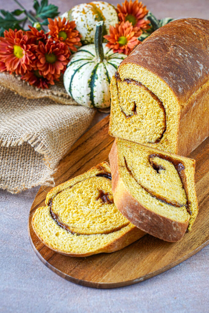 Pumpkin Cinnamon Swirl Bread on a wooden board with two cut slices.
