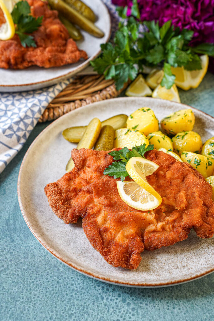 Close up of Smažený Vepřový Řízek (Czech Breaded Pork Cutlet) on a plate with a lemon slice and parsley sprig.