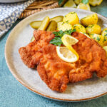 Smažený Vepřový Řízek (Czech Breaded Pork Cutlet) on a plate with lemon, parsley, pickles, and parsley potatoes.