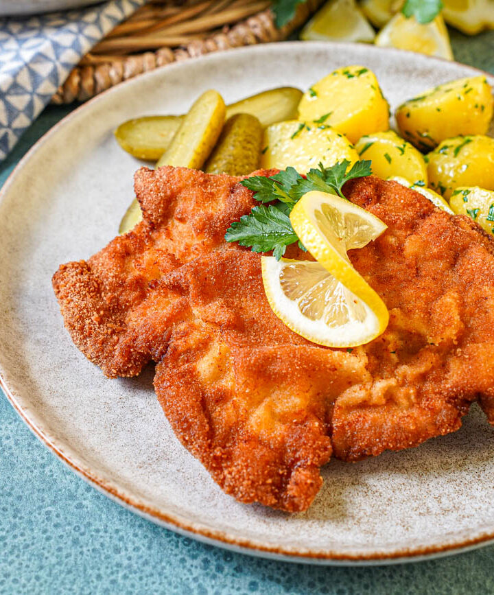 Smažený Vepřový Řízek (Czech Breaded Pork Cutlet) on a plate with lemon, parsley, pickles, and parsley potatoes.