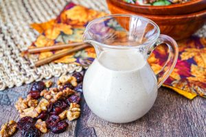 Maple Walnut Vinaigrette in a glass container next to walnuts and cranberries.