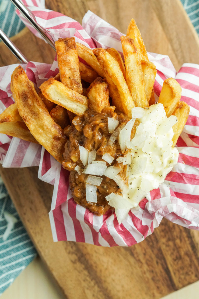 Aerial view of Patatje Oorlog (Dutch War Fries) with sate sauce, raw onions, and mayonnaise in a red and white striped liner
