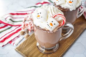 Close up of Peppermint Eggnog Hot Chocolate in two clear mugs with snowman marshmallows.