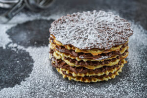 A stack of Pizzelle (Italian Waffle Cookies) covered in powdered sugar.