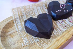 Two Strawberry Balsamic Chocolates in heart shapes on a wooden board.