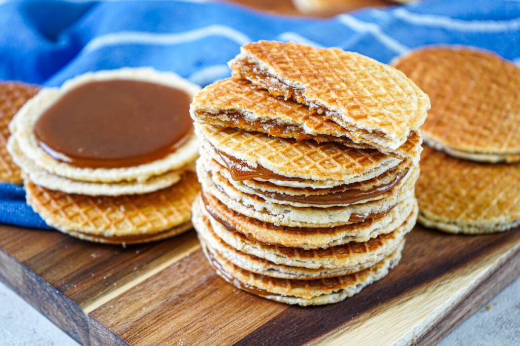 A stack of Stroopwafels (Dutch Syrup-Filled Waffle Cookies) on a wooden board next to a blue towel.