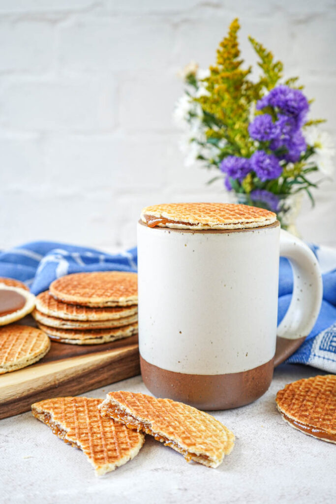 Side view of Stroopwafels (Dutch Syrup-Filled Waffle Cookies) next to a mug with one resting on top.