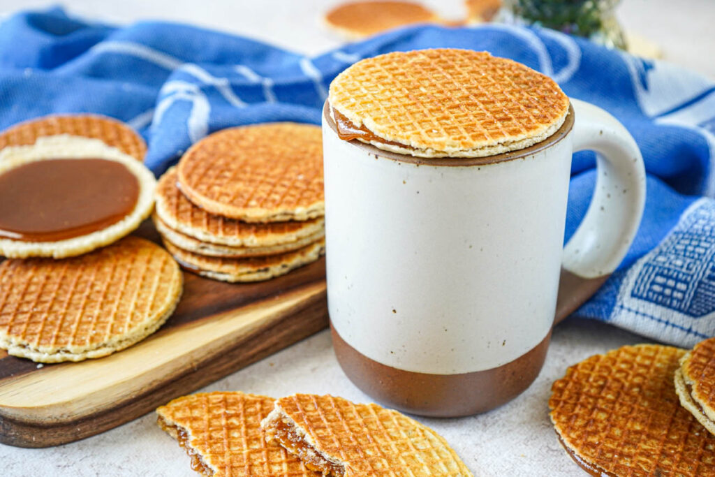 Stroopwafels (Dutch Syrup-Filled Waffle Cookies) next to white and brown mug with one resting on top of the mug.