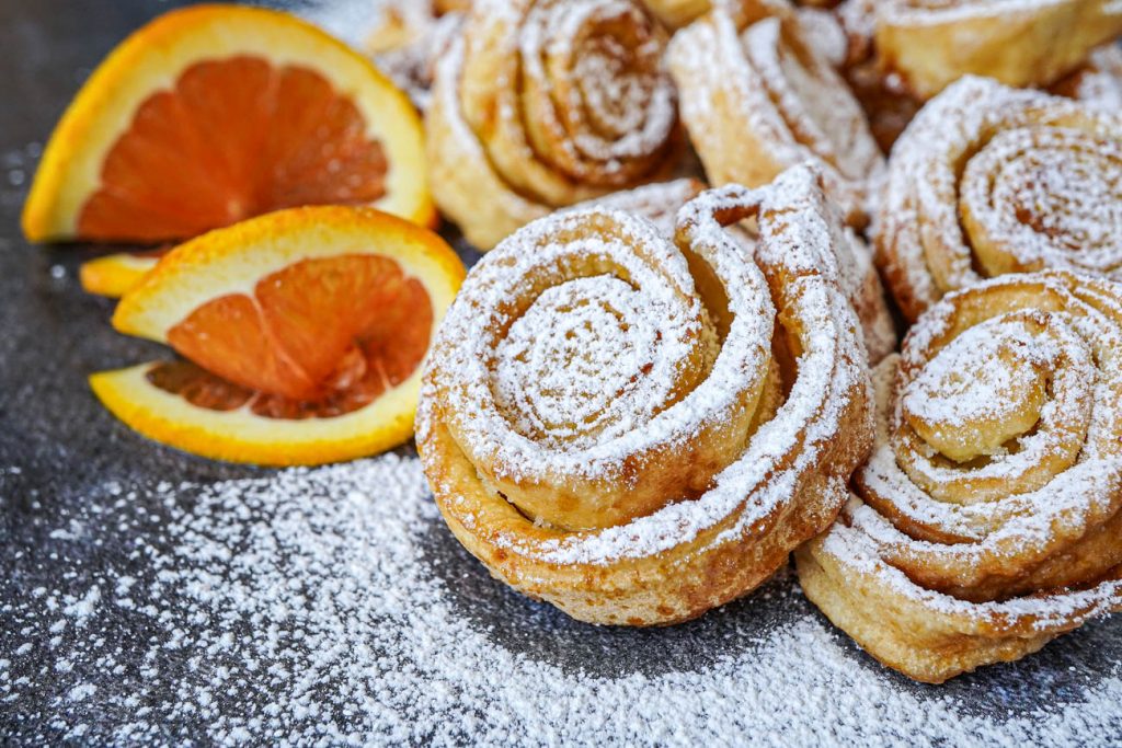 Tagliatelle Dolci di Carnevale (Italian Carnival Sweet Tagliatelle) covered in powdered sugar and next to orange slices.
