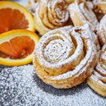Tagliatelle Dolci di Carnevale (Italian Carnival Sweet Tagliatelle) covered in powdered sugar next to orange slices.