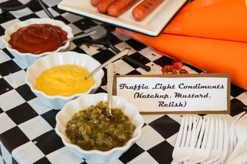 Relish, mustard, and ketchup in three white bowls with sign- Traffic Light Condiments.