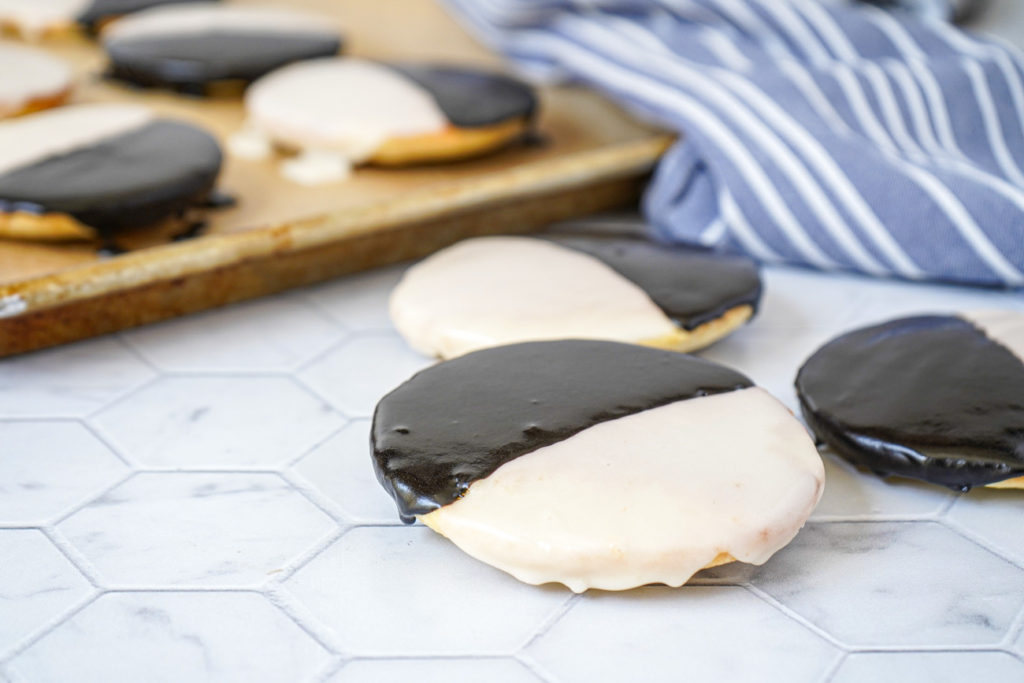 Three Black and White Cookies with more in the background on a baking sheet.