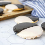 Black and White Cookies with more in the background on a baking sheet.