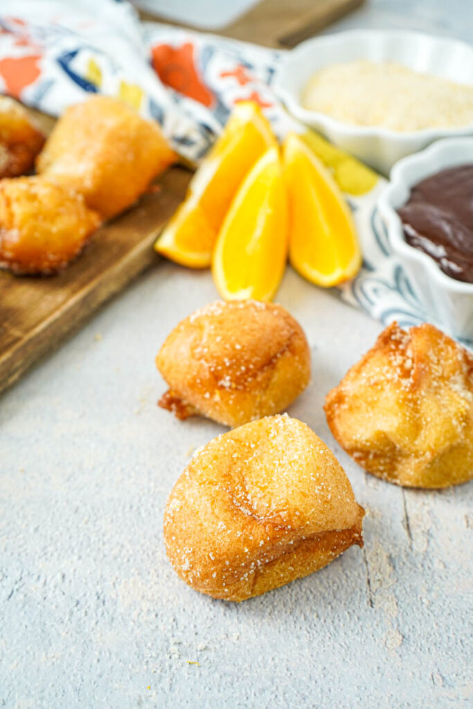 Three Buñuelos with Brown Velvet Glaze with orange slices and sugar in the background.