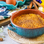 Encharcada (Portuguese Soaked Eggs) in a bowl next to lemon slices and cinnamon sticks.