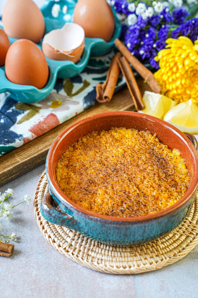 Encharcada (Portuguese Soaked Eggs) in a clay bowl next to eggs, cinnamon sticks, lemon wedges, and flowers.