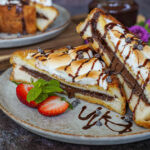 Two S'mores French Toast halves on a plate with strawberries, mint sprigs, and chocolate sauce.