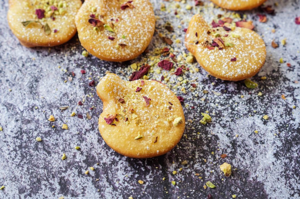 Scattered Afghani Gosh-e-Fil (Elephant Ear-Shaped Fried Pastry) topped with rose petals and crushed pistachios.