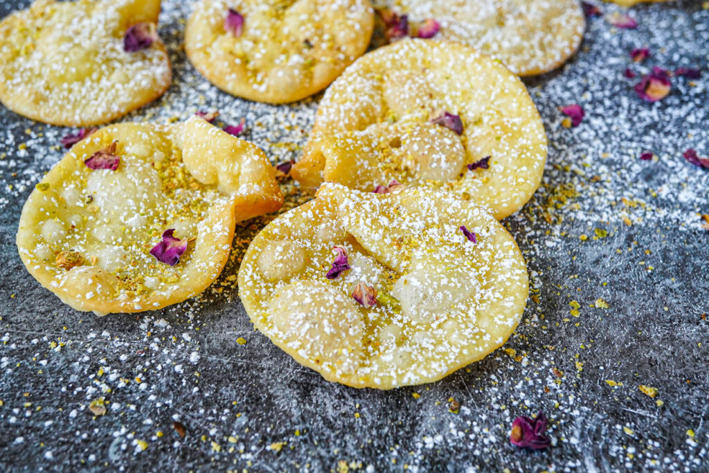 Close up of Gosh-e-Fil (Elephant Ear-Shaped Fried Pastry) topped with powdered sugar, ground pistachios, and rose petals.