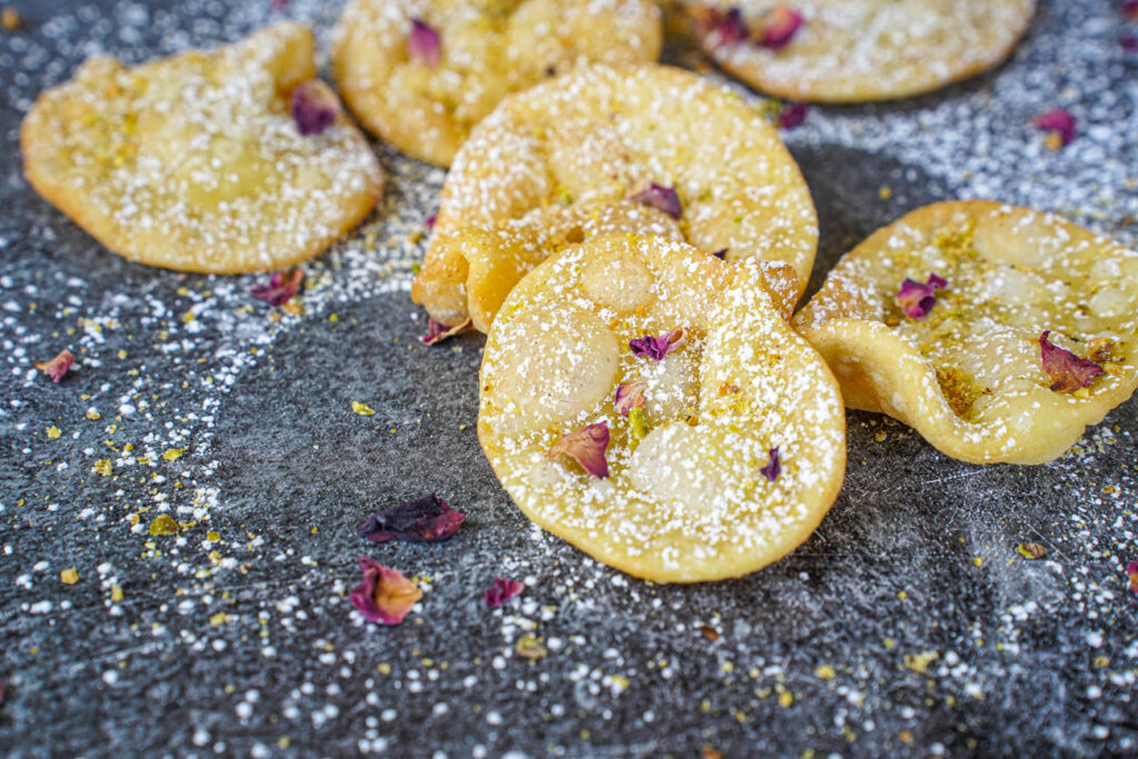 Gosh-e-Fil (Elephant Ear-Shaped Fried Pastry) dusted with powdered sugar, ground pistachios, and rose petals.
