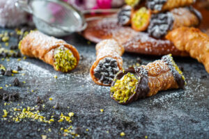 Three homemade cannoli dusted with powdered sugar with more in the background on a wooden board.