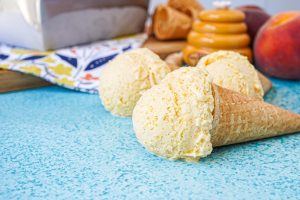 Three scoops of Honey Peach Ice Cream with cones on a blue surface.