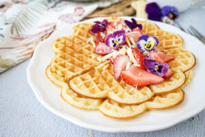 Two Prosecco Waffles on a white plate with strawberries, white chocolate, and flowers.